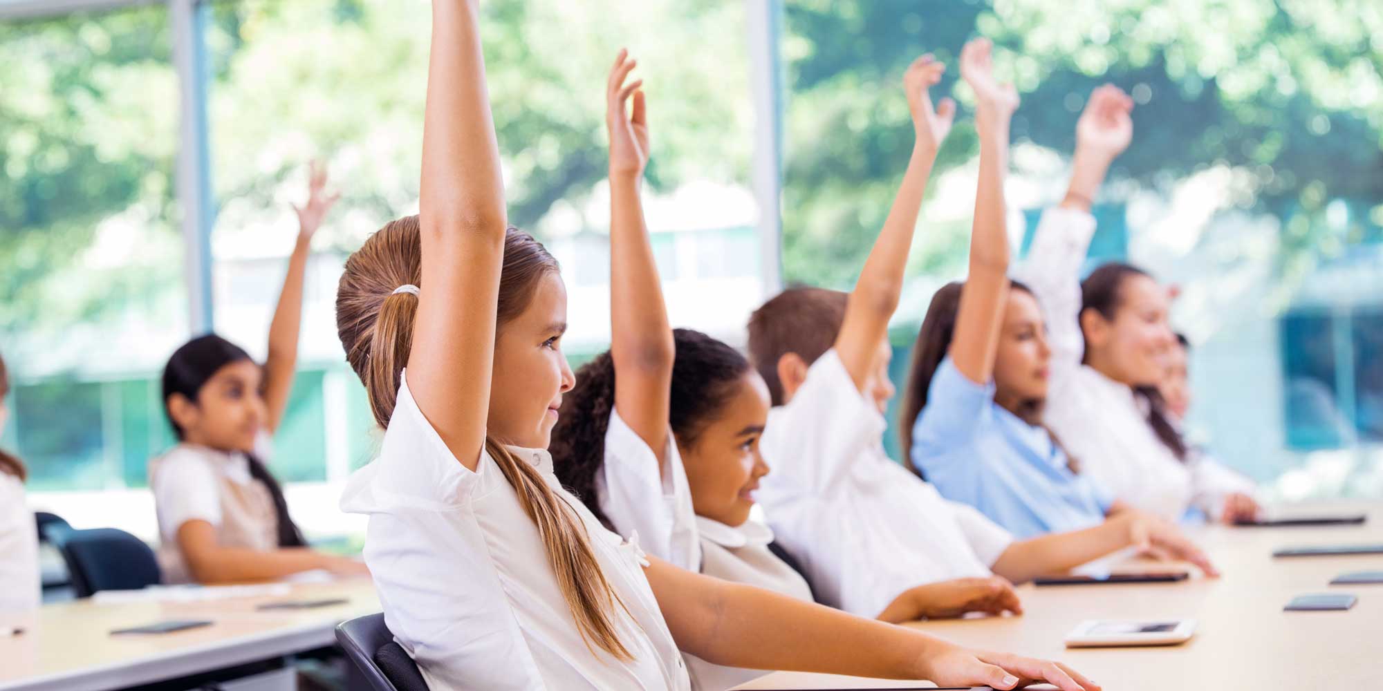 Students at their desks raising their hands in class.